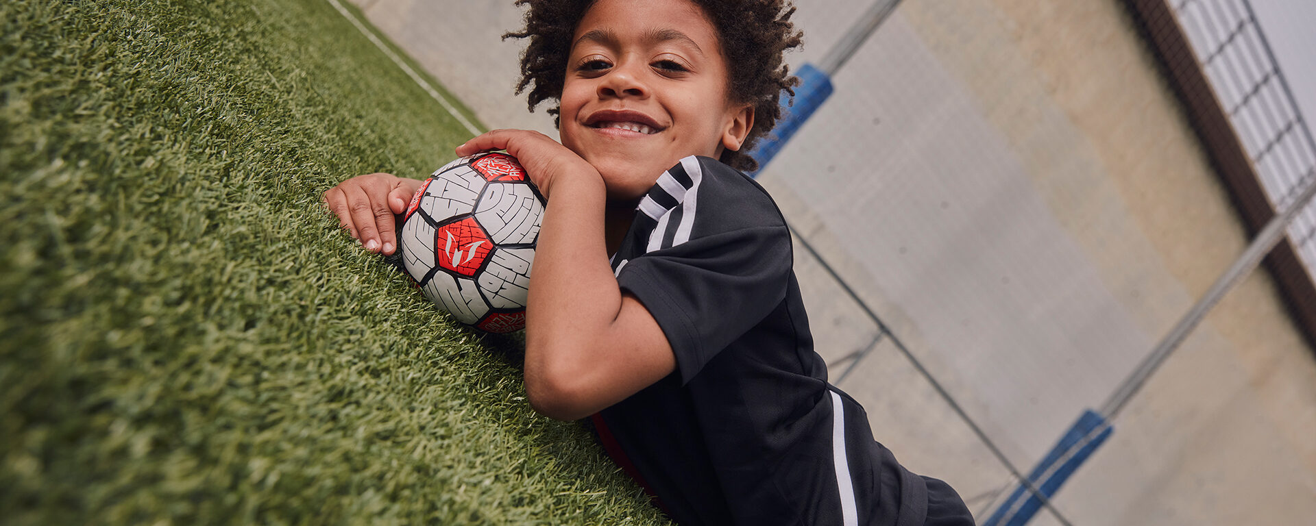 Niño acostado en la hiera con un balón de fútbol bajo su mentón